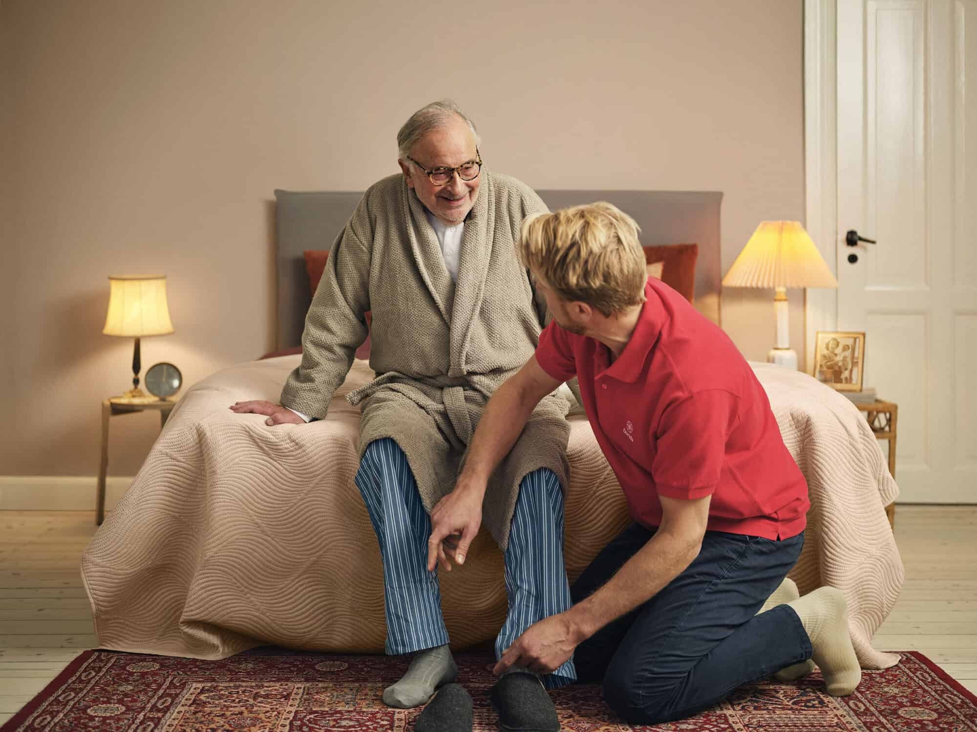 A personal caregiver assists an elderly man in putting on his shoes, representing the essence of home help services 